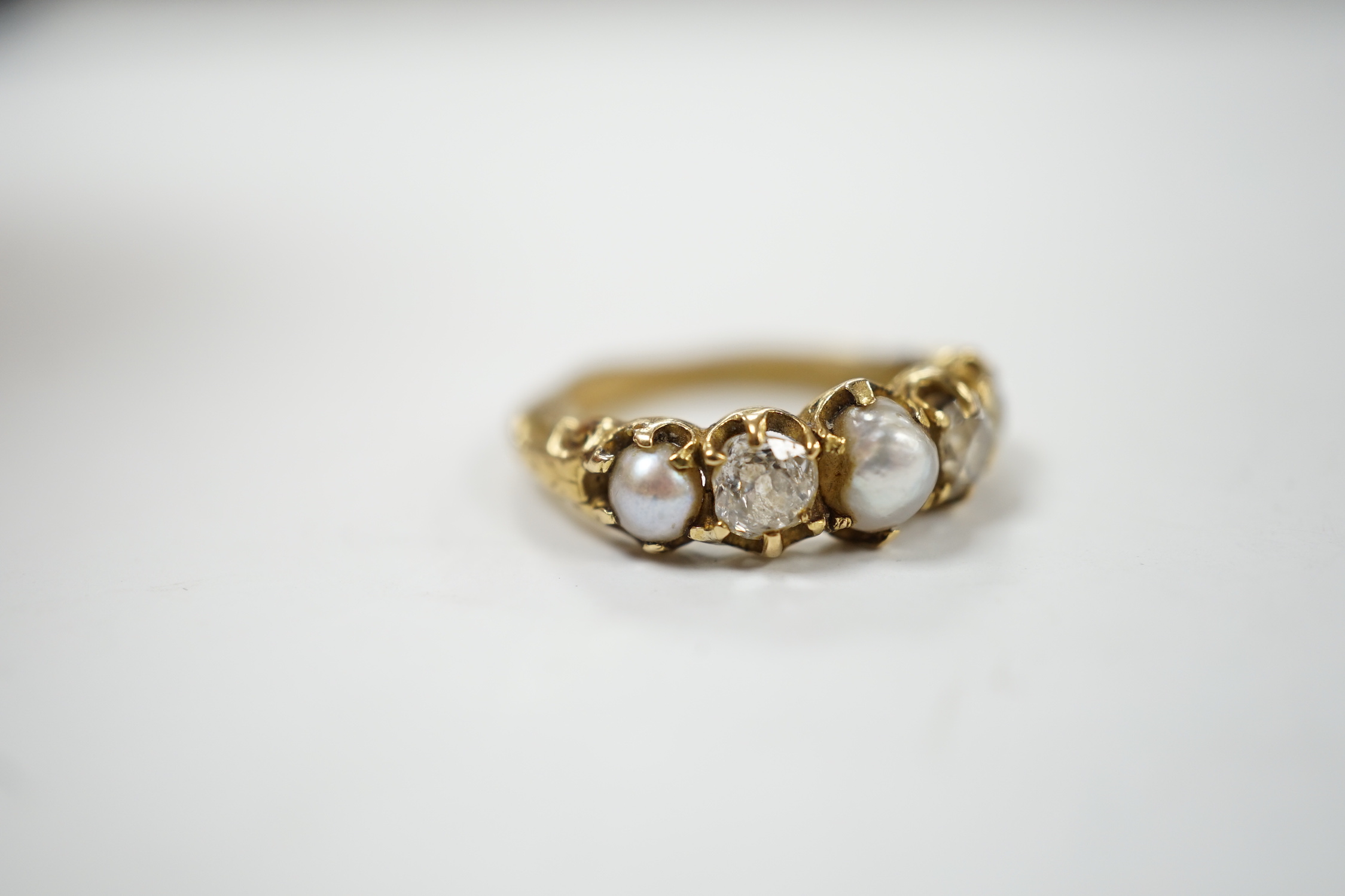A late Victorian yellow metal and graduated three stone split pearl and two stone diamond set half hoop ring, with unusual wax? insert to the shank, size F, gross weight 3.2 grams.